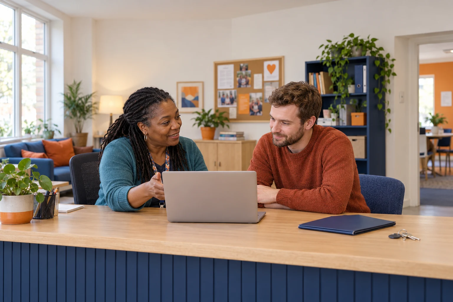 Two adults reviewing a laptop at a community centre reception desk.